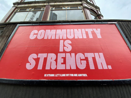 A large red billboard with white text reading COMMUNITY IS STRENGTH on a building. strength routines and mindset shift
