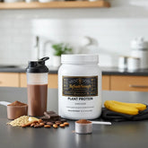 Chocolate plant protein powder with shaker, bananas, and nuts for muscle recovery and wellness