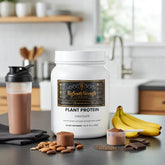 Chocolate plant protein powder with shaker, bananas, almonds, and chocolate pieces on kitchen counter